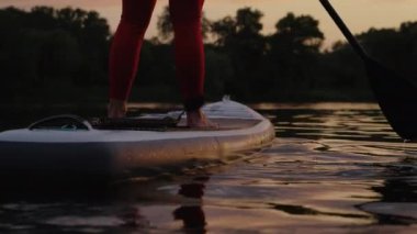 Gün batımında sörf tahtasında kadın bacakları