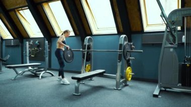 Formda bir kadın halterin üzerine ağırlık koyuyor.