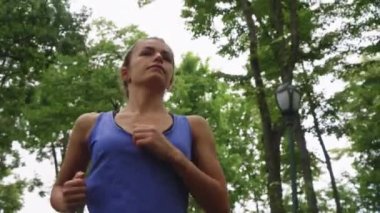 Atletik kadın yavaş çekimde ağaçların altında koşuyor.