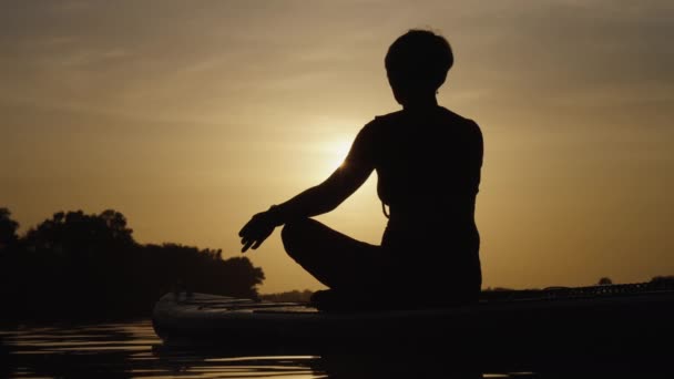 Silhueta de mulher praticando ioga na prancha SUP ao pôr do sol — Vídeo de Stock