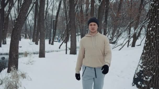 Hombre en ropa deportiva caminando en el parque cubierto de nieve — Vídeos de Stock