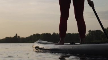 Gün batımında SUP tahtasında kürek çeken kadın bacakları