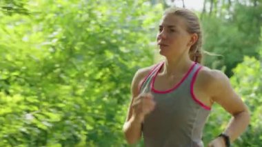 Formda bir kadın ağır çekimde parkta koşuyor.