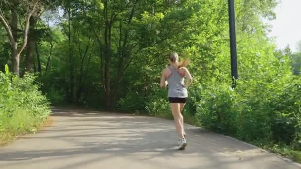 Подтянутая женщина бегает в солнечном парке в замедленной съемке — стоковое видео