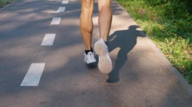 Yavaş çekim erkek bacakları güneşli bir sabahta yolda koşuyor.