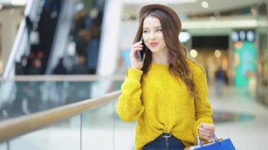 Alışveriş merkezinde yürüyen ve telefonla konuşan mutlu bir kadın.