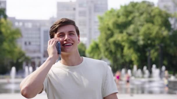 Uomo sorridente che parla al telefono mentre cammina in città — Video Stock