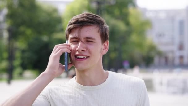 Happy young man talking on phone during city walk — Stock Video