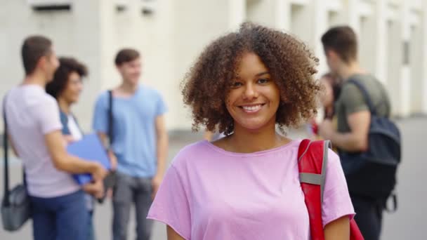 Negro chica estudiante sonriendo en cámara cerca de la universidad edificio — Vídeo de stock