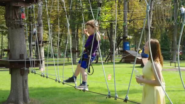 Boy climbing rope trail while mom giving him moral support — Stock Video
