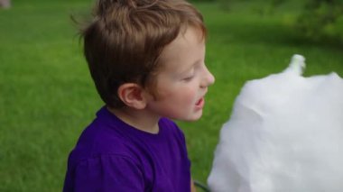 Kızıl saçlı çocuk parkta pamuk şeker yiyor.