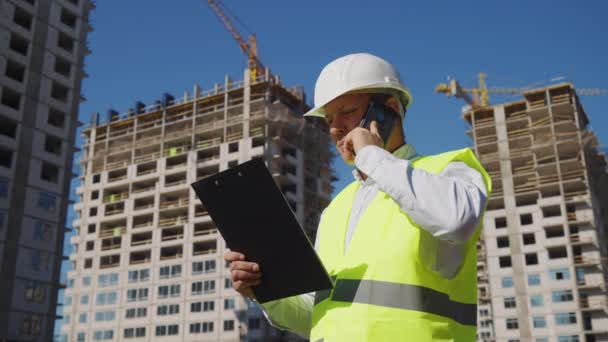 Capataz de revisar los planes y hablar por teléfono en el sitio de construcción — Vídeos de Stock