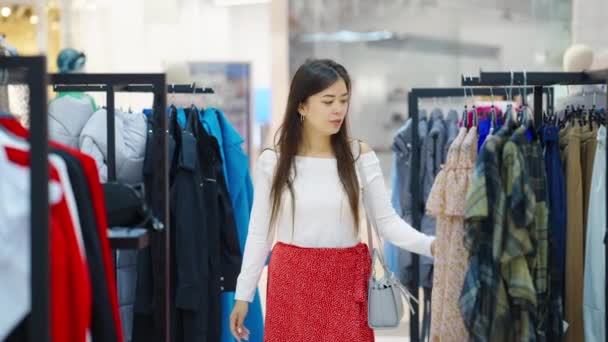 ファッション店で買い物をしながら服に触れるアジアの女性 — ストック動画