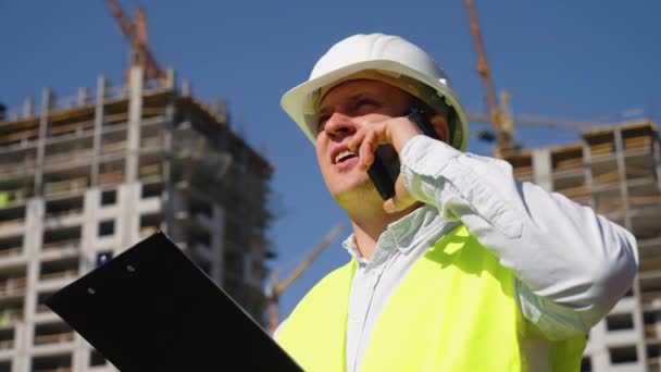 Byggnadsinspektör talar i telefon på byggarbetsplatsen — Stockvideo