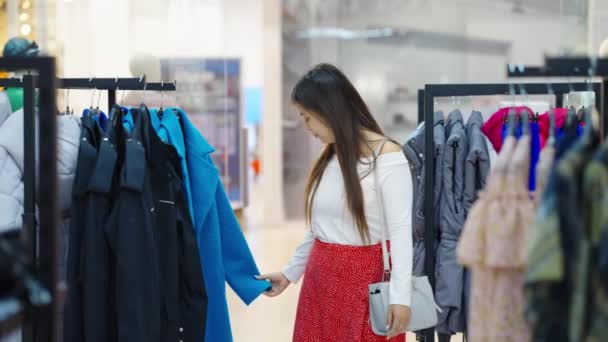 Mujer asiática eligiendo trajes elegantes en la tienda de ropa — Vídeo de stock