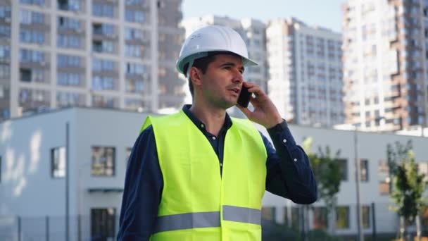 Contratista del edificio hablando por teléfono contra el nuevo distrito de la ciudad — Vídeos de Stock