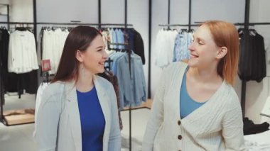 Başarılı bir alışveriş gezisinden sonra elinde renkli alışveriş çantaları tutan iki kadın, modern giyim mağazasında perakende terapinin keyfini çıkarıyorlar.