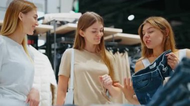 Üç kadın moda mağazasında konuşurken, biri kot pantolon, ortak stil ve perakende karar verme kavramı gösteriyor.