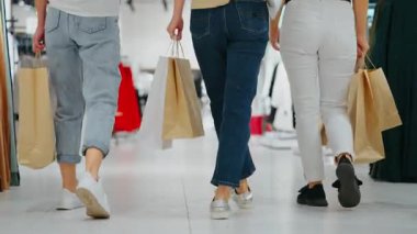 Üç kadın, ellerinde kağıt torbalarla moda mağazasına doğru yürüyorlar. Düşük açılı yakın çekim, ortak alışveriş seyahati ve modern perakende satış kavramı.