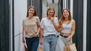 Üç kadın alışveriş merkezinin koridorunda alışveriş çantalarıyla yan yana yürüyor gülümsüyor ve konuşuyor, yaşam tarzı ve kadın arkadaşlığı kavramı.