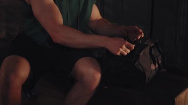 Kapüşonlu ve şortlu atletik adam spor çantalarını açıp boks antrenmanından önce soyunma odasındaki kırmızı sargıları çıkarıyor.