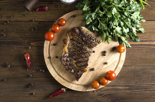 Cooked beef steak on wooden board on wooden background — Stock Photo, Image