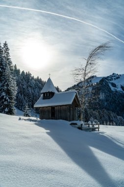 Alp tarlalarında karlı şapeli olan kış harikalar diyarı. Ormanın kenarındaki karlı ağaçlar ve Avusturya dağları karla kaplandı. Vorarlberg Alpleri, Bregenz ormanında. bulutlu güneşli bir gün