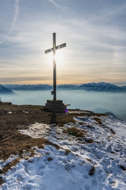 Karlı dağın zirvesinde çaprazlı panorama, güneş yıldızlı ahşap haç, zirveye giden yol, örtülü siluet arka plan, güneşli kış gününde güneşli bir kış günü Rheintal 'den Sntis' e manzaralı paskalya yürüyüşü.