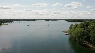 Bir dron, Litvanya 'daki Trakai Gölü' nün sakin sularında soldan sağa hareket eden bir yelkenli yarışmasının heyecan verici görüntüsünü yakalıyor..