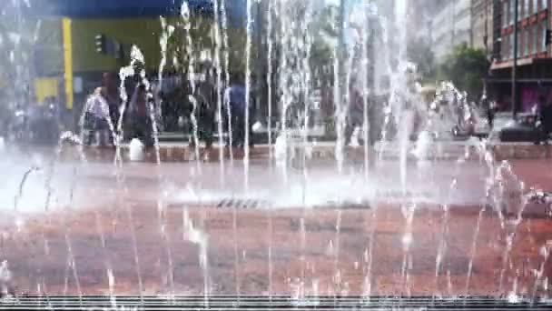 Busy street on a hot summer day, people walk past fountain with refreshing water — Stock Video
