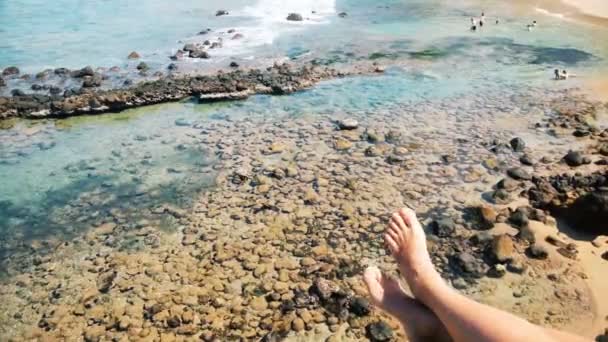 Urlaub, weibliche Füße bewegen sich spielerisch am felsigen Meeresstrand, Menschen schwimmen — Stockvideo