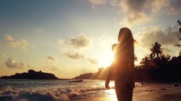 Jonge vrouw kijken naar zonsondergang op tropisch strand, stormachtige oceaan golven zand wassen — Stockvideo