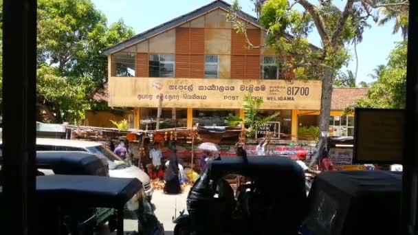 Weligama, Sri Lanka - Circa febrero 2016: Los peatones y el tráfico en la calle. Ocupada calle con coches, tuk tuks, peatones pasando por la oficina de correos y el mercado — Vídeo de stock