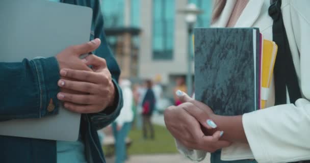 Dos estudiantes universitarios sosteniendo cuadernos y laptop, hablando afuera, educación — Vídeo de stock