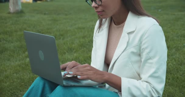 Pretty female typing email, sitting on grass, working in park, online business — Stock video