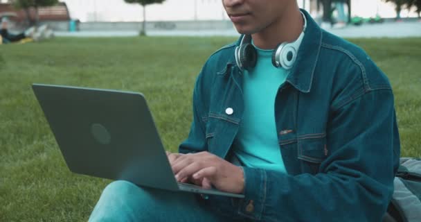 Hombre estudiante universitario escribiendo ensayo en el ordenador portátil, sentado en el parque, la educación moderna — Vídeo de stock