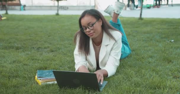 Młoda, zrelaksowana kobieta komunikująca się w sieciach społecznościowych, pisząca na laptopie w parku — Wideo stockowe