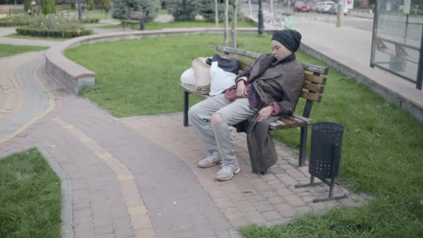 Mujer joven sin hogar durmiendo en el banco en el parque, problema social, pobreza — Vídeos de Stock