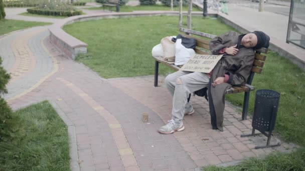 Γυναίκα βάζει χρήματα σε κύπελλο επαιτείας, βοηθώντας άστεγη γυναίκα, κοιμάται στο πάρκο — Αρχείο Βίντεο