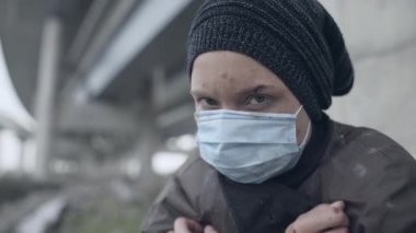 Koruyucu maskeli evsiz bir kadın öksürüyor, kameraya bakıyor, tehlikeli bir virüs.