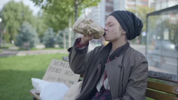 Бідна молода жінка п'є алкоголь, сидячи на лавці, шкідлива залежність — стокове відео