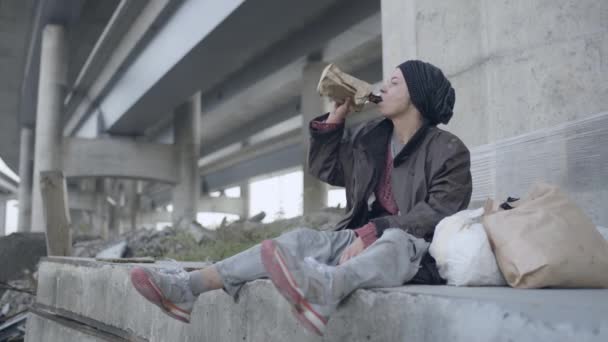 Depressed female refugee drinking alcohol under the bridge, social exclusion — Stock Video