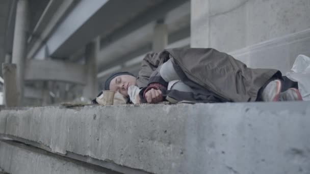 Vrouwelijke vluchteling bedekt met vuile jas slapen onder de brug, werkloosheid — Stockvideo