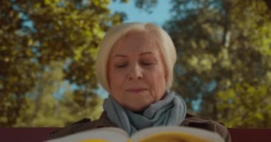 Yaşlı kadın dışarıda ilginç kitaplar okuyor, emeklilikte boş vakit geçiriyor.