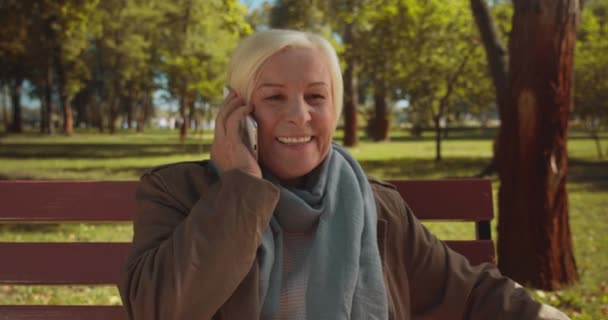 Mulher madura feliz falando no telefone, sentado no banco no parque, comunicação — Vídeo de Stock