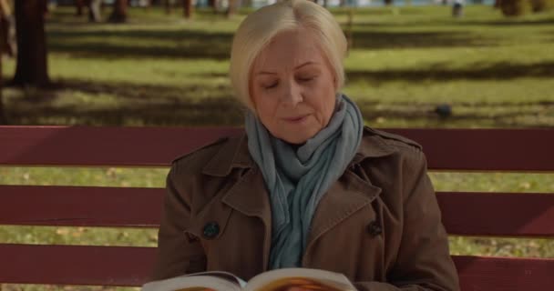 Atraente livro de leitura feminina de meia-idade, relaxante no banco no parque, conhecimento — Vídeo de Stock