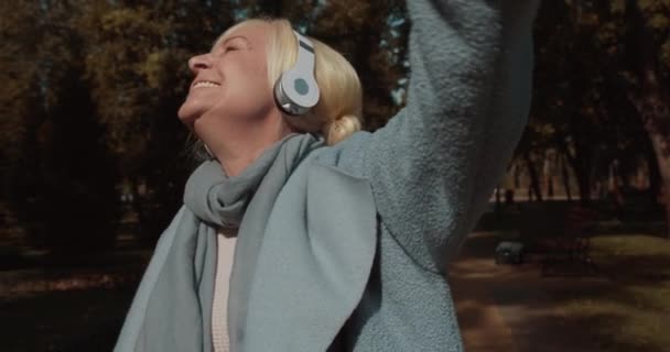 Mujer rubia activa en auriculares bailando al aire libre, pensionista femenina feliz, diversión — Vídeos de Stock