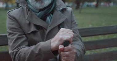 Bastona yaslanan, parkta buluşmayı bekleyen, gergin bir adam.