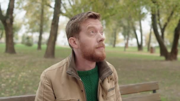 Fiatal megfontolt férfi ül a padon a parkban, aggódva a problémák miatt — Stock videók