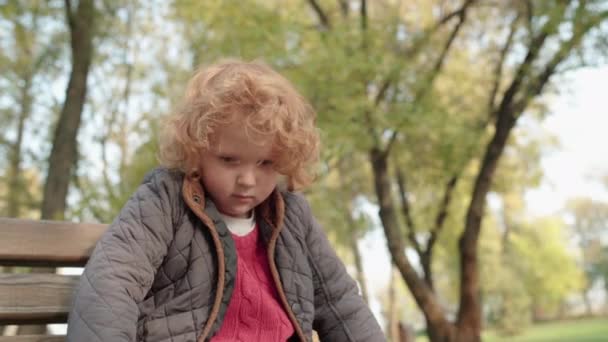 Verärgerter rothaariger Junge sitzt auf Bank, fühlt sich einsam, beleidigtes Kind, Pflege — Stockvideo